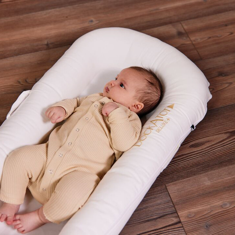 赤ちゃんがDockATot（プリスティンホワイト）で眠っている様子｜木目フロア背景