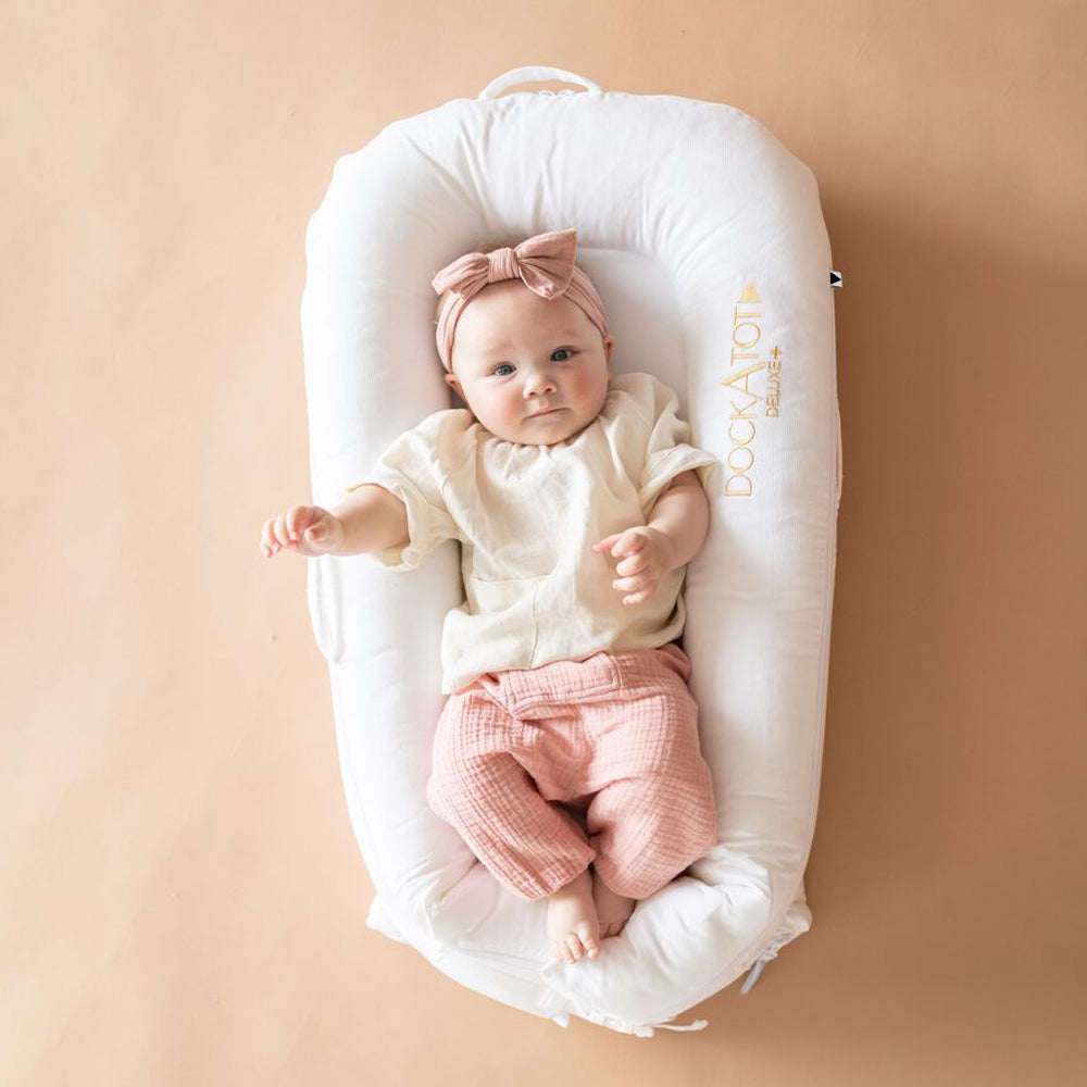 DockATot（プリスティンホワイト）で赤ちゃんがリラックスしている様子（ピンク背景）